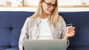 a woman sitting on a couch with a laptop and smiling at the camera